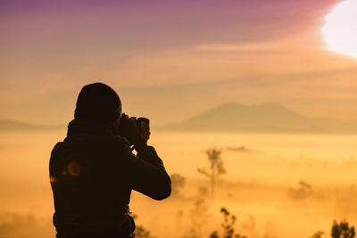 Silhouette person photographing against sky during sunset