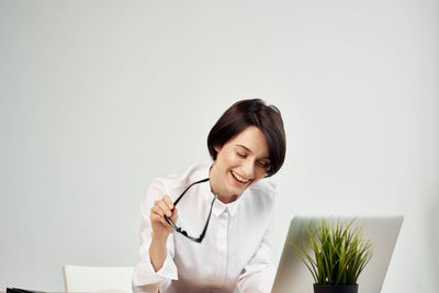 Young woman smiling while sitting on table against white background