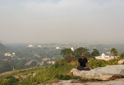 Man sitting on rock looking at cityscape against sky