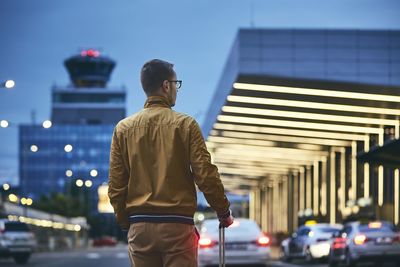 Rear view of man standing against illuminated city