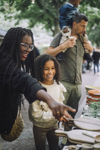 Smiling mother pointing near daughter while doing shopping at flea market