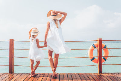 Rear view of woman wearing hat standing on pier against sea against sky