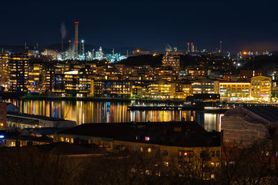 Illuminated buildings by river against sky at night