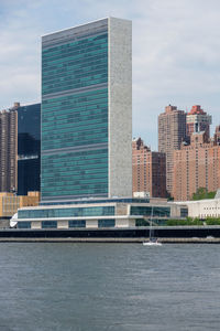 Modern buildings by river against sky in city