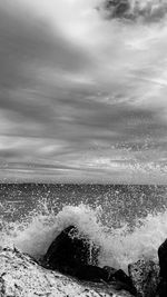 Sea waves splashing on shore against sky