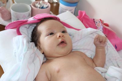 Close-up of shirtless baby girl lying on bed