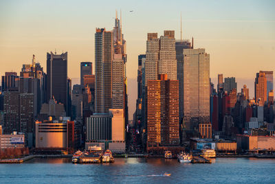 Sea by buildings against sky during sunset