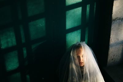 High angle view of depressed bride wearing veil by window