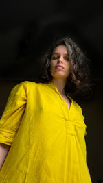 Portrait of woman looking away while standing against black background