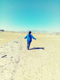 Rear view of man standing on beach against clear blue sky