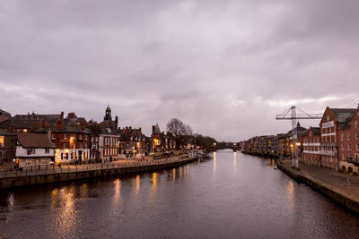 Illuminated buildings by river against sky in city