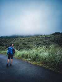 Rear view of man walking on dirt road against sky