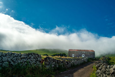 Empty road leading towards old house against cloudy sky