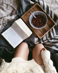 Midsection of woman with book and pomegranate seeds on bed at home