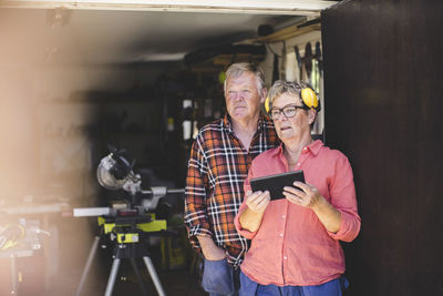 Thoughtful senior couple with digital tablet looking away while standing at workshop doorway