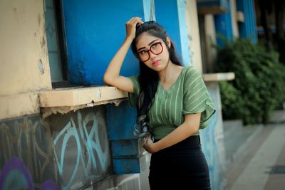 Portrait of young woman standing against wall