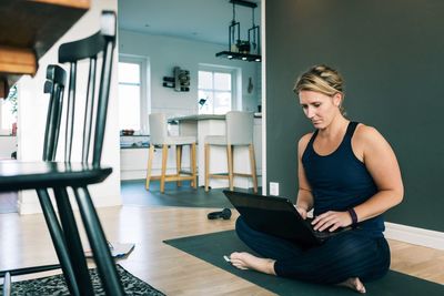 Woman working over laptop while sitting on mat in living room at home
