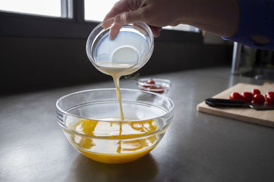 Pouring milk into egg batter, sliced tomatoes in background.