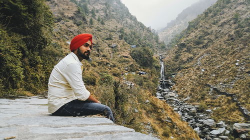 Side view of young man sitting on rock