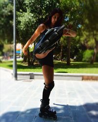 Portrait of young woman kicking while roller skating at park on sunny day