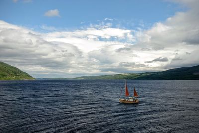 Sailboat sailing in sea against cloudy sky