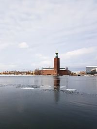 Lighthouse on river by buildings against sky