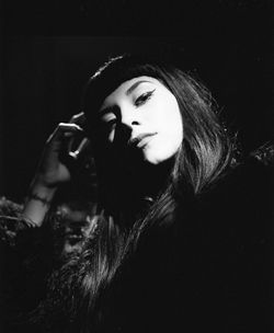 Close-up portrait of young woman standing against black background