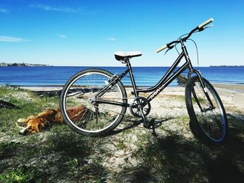 Bicycle parked by sea against blue sky