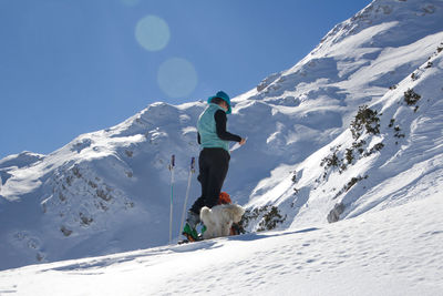 Full length of woman holding paper while walking by dog on snow covered mountain against sky