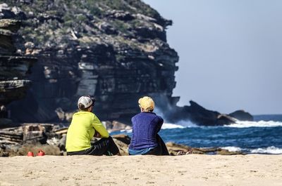 Rear view of people sitting on rock by sea