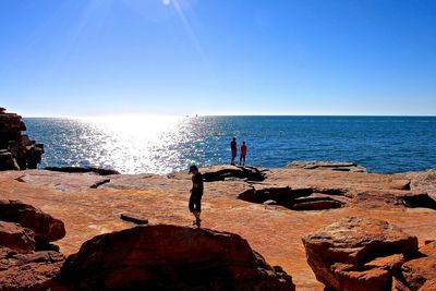 People on rocky sea shore against clear blue sky during sunny day