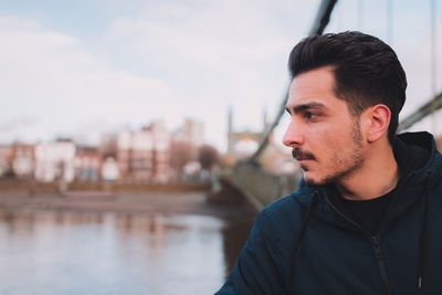 Close-up of thoughtful young man standing by river in city