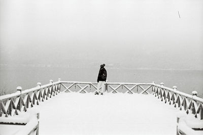 Man standing on railing by sea against sky