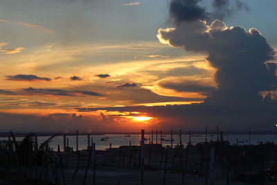 Silhouette city by sea against sky during sunset