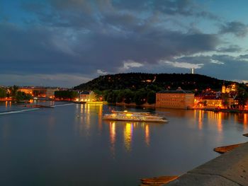 Illuminated buildings by sea against sky at sunset