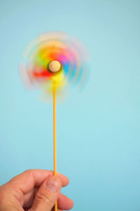 Close-up of hand holding spinning pinwheel toy over blue background