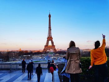 Rear view of people looking at eiffel tower in city against sky during sunset