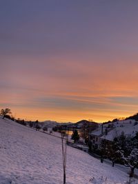 Snow covered field against sky during sunset