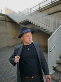 Man smoking cigarette while standing against staircases