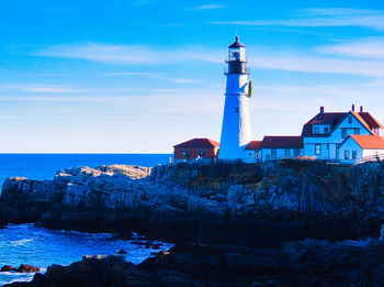 Lighthouse by sea and buildings against sky