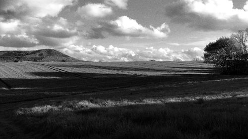 Dirt road on grassy field against cloudy sky