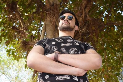 Portrait of young man wearing sunglasses standing against trees