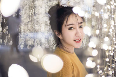 Portrait of smiling young woman amidst illuminated string lights