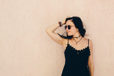 Young woman wearing sunglasses standing against wall