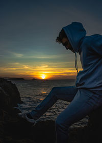 Rear view of man standing at beach against sky during sunset