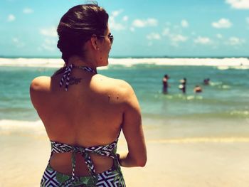 Rear view of woman standing on shore at beach against sky