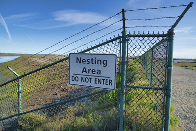 Information sign on fence against sky