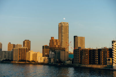 Modern buildings by river against sky in city