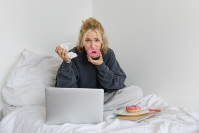 Portrait of young woman using mobile phone while sitting on bed at home