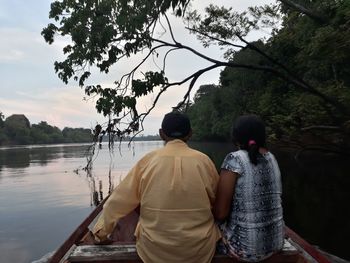 Rear view of people sitting by lake against sky